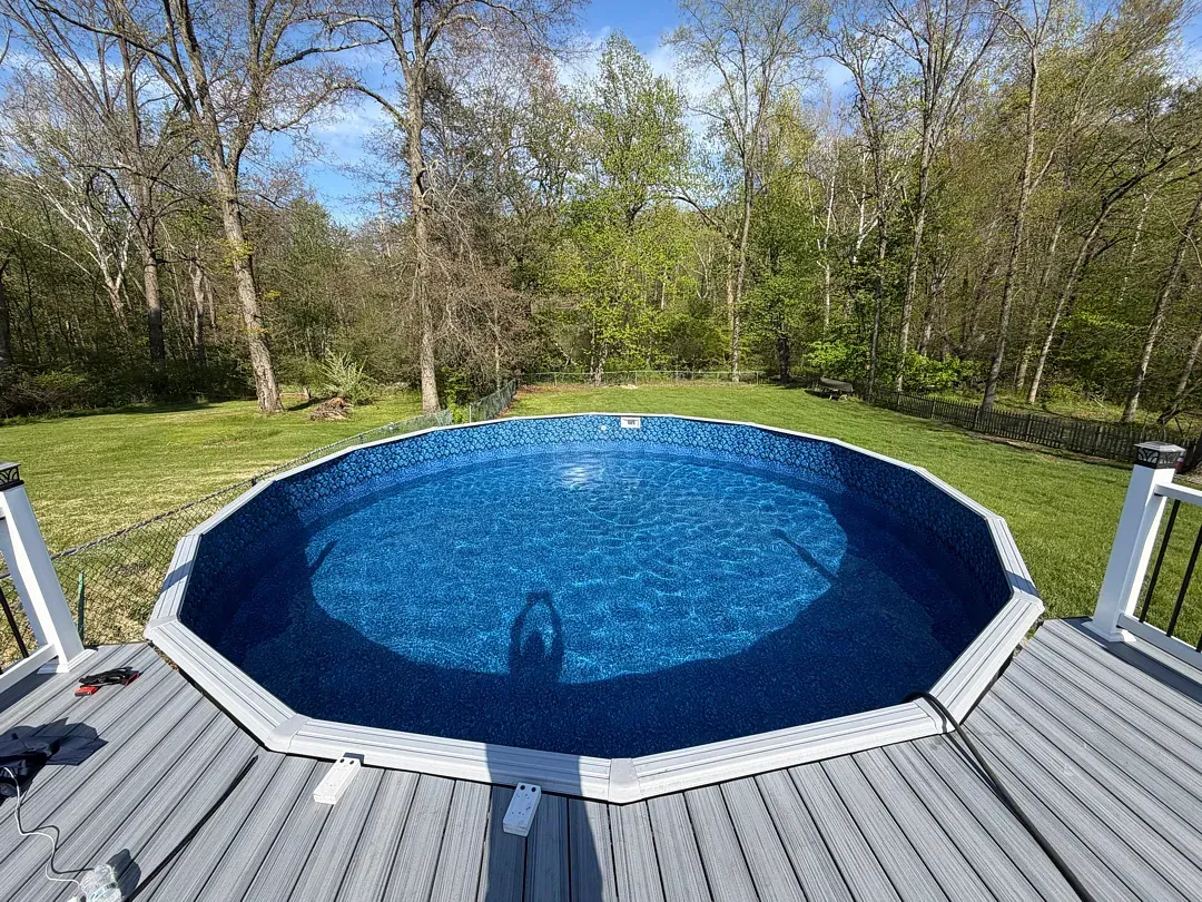 Backyard pool with blue water on a wooden deck, surrounded by trees and grass