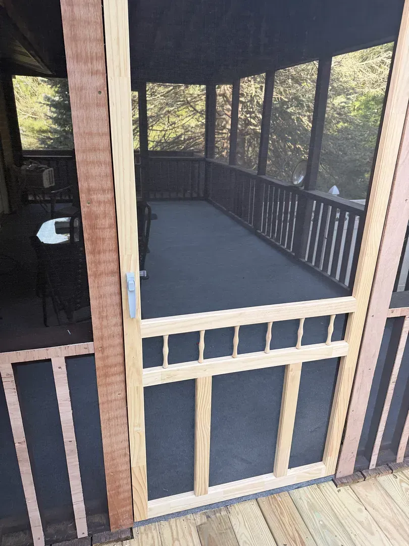 Screened porch with railing and gray floor, viewed through a door.