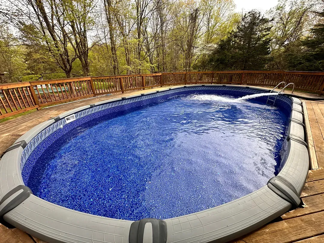 Empty blue swimming pool with a gray cover, surrounded by a wooden deck and trees