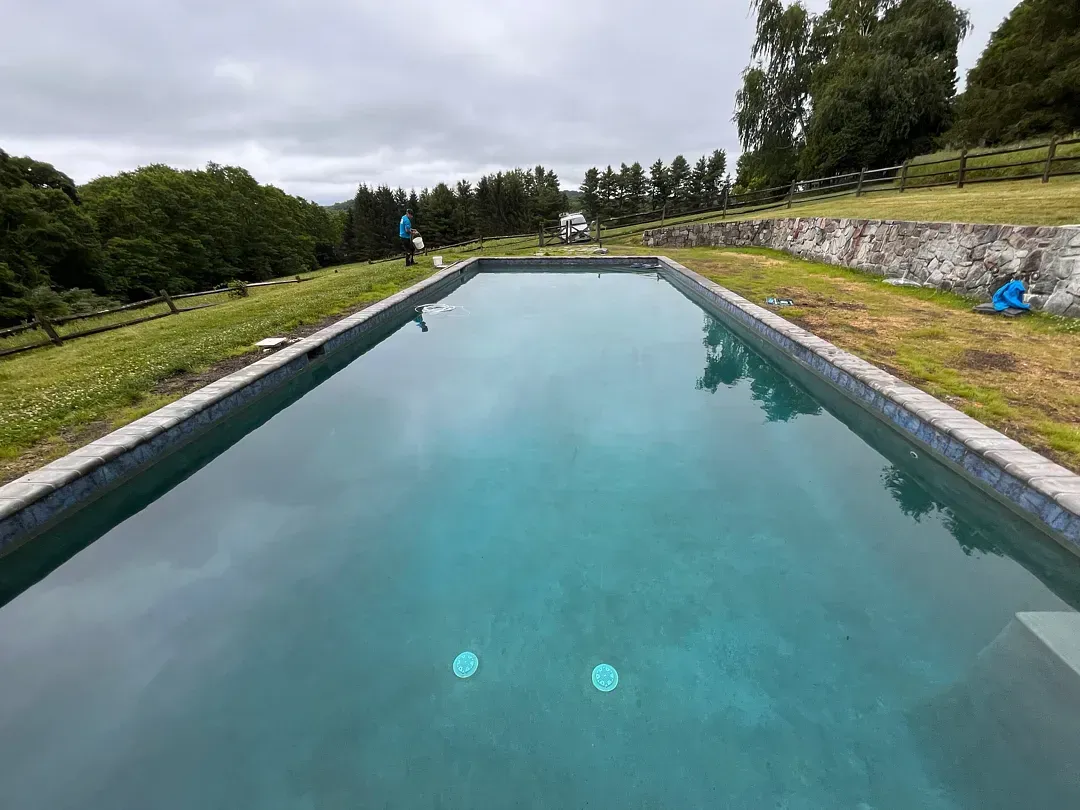 Long rectangular outdoor pool with turquoise water, surrounded by grassy embankments and trees
