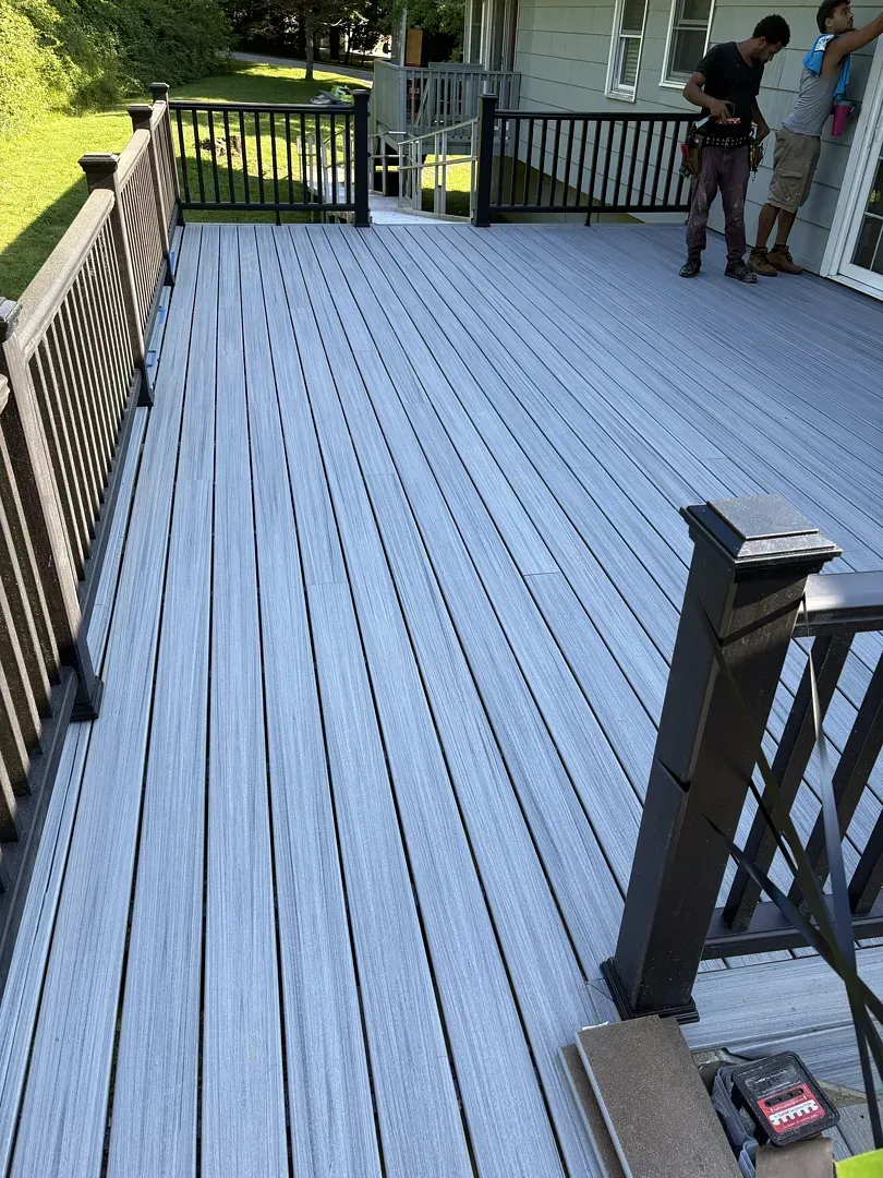 Wooden deck with black railings and two people standing near a house in the background