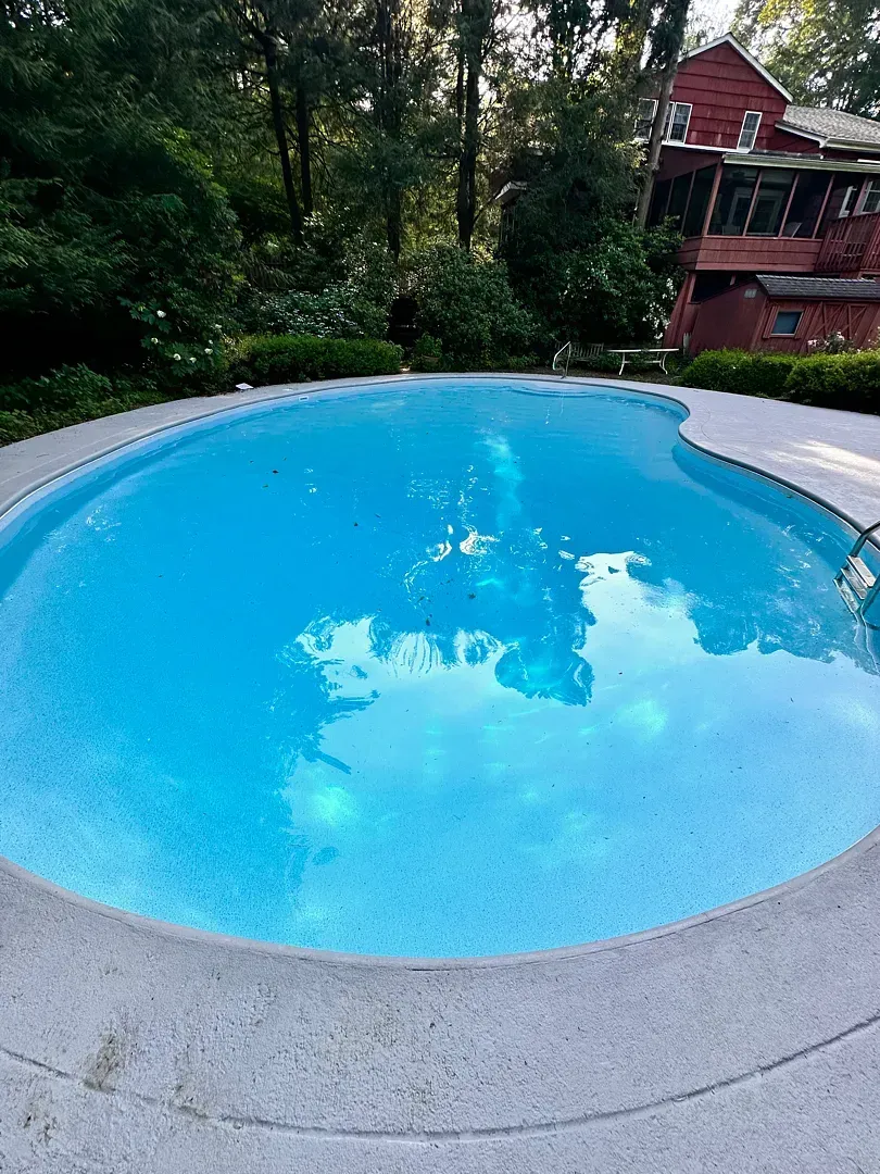Round blue swimming pool surrounded by trees and a brick house in the background