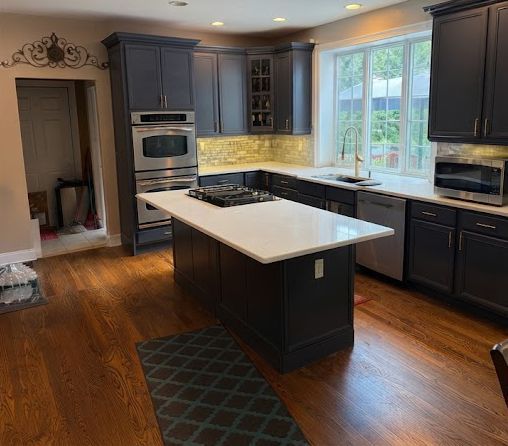 Modern kitchen with dark cabinets, white island, hardwood floors, and large window