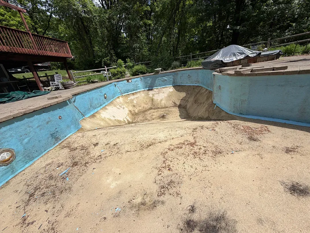 Empty drained swimming pool with peeling blue walls in a wooded outdoor area