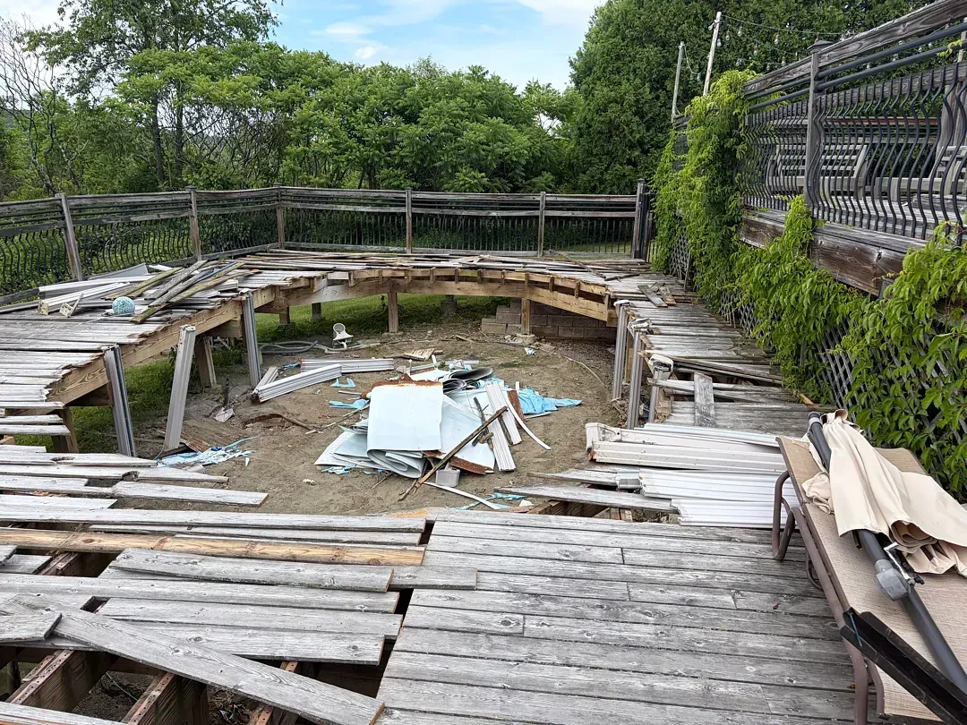 Empty, weathered wooden pool deck with a drained circular pool and overgrown greenery around it