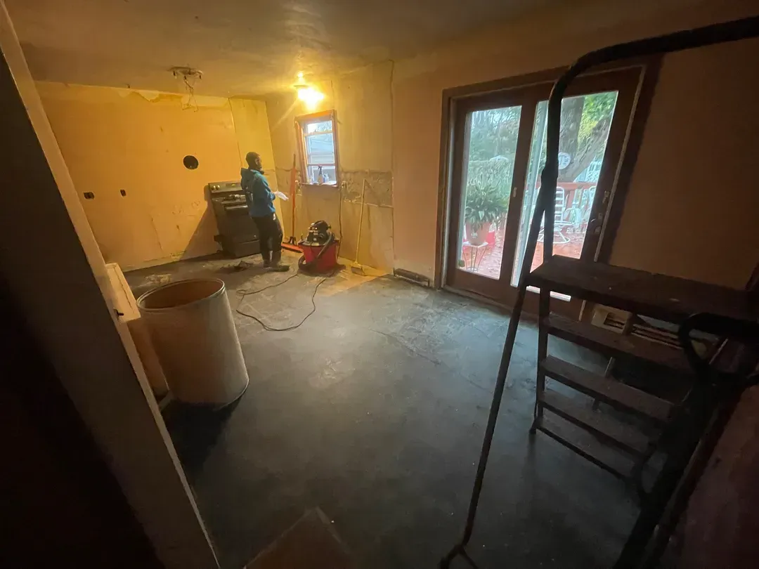 Partially renovated room with tools, ladder, yellow walls, and sliding glass doors opening to greenery