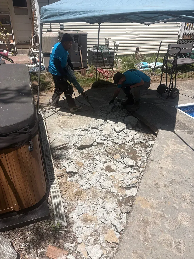 Workers smoothing fresh concrete in a small outdoor patio area beside a house.
