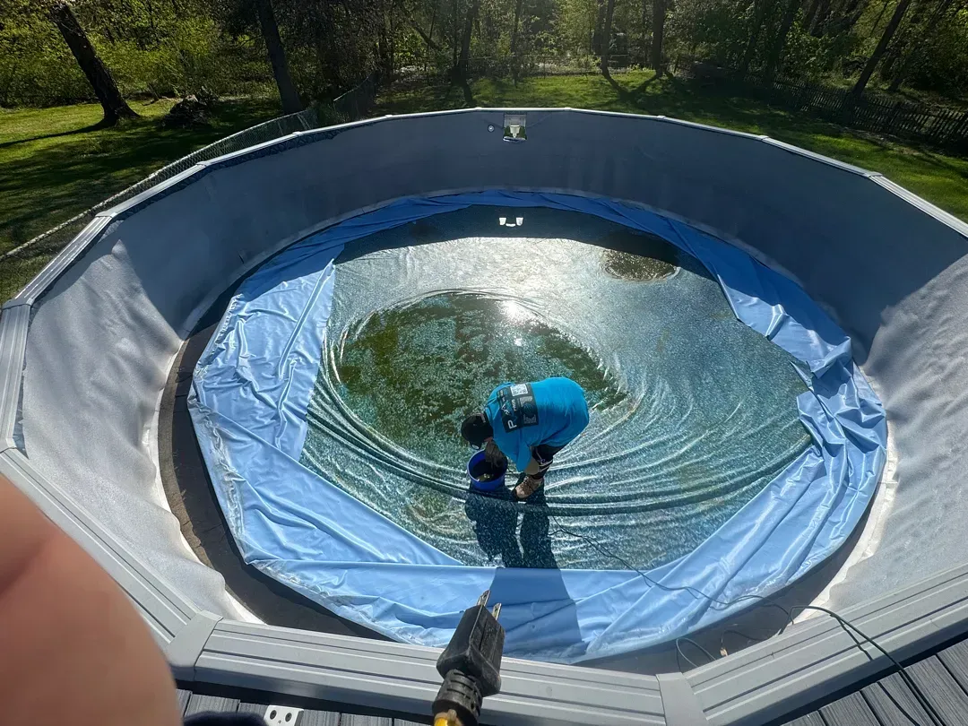 Blue pool liner being cleaned inside an above-ground pool in a sunny backyard