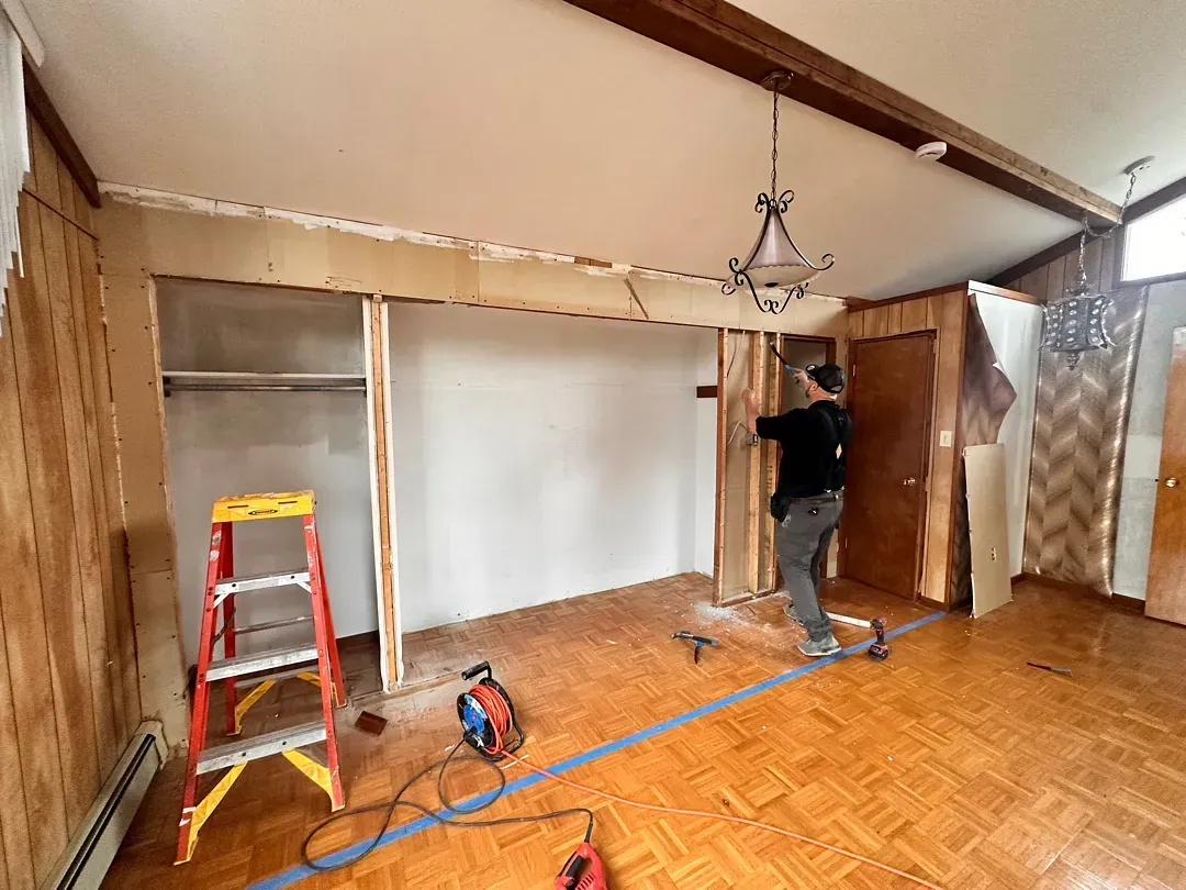 Person renovating a room with a ladder, tools, and exposed wall area under repair