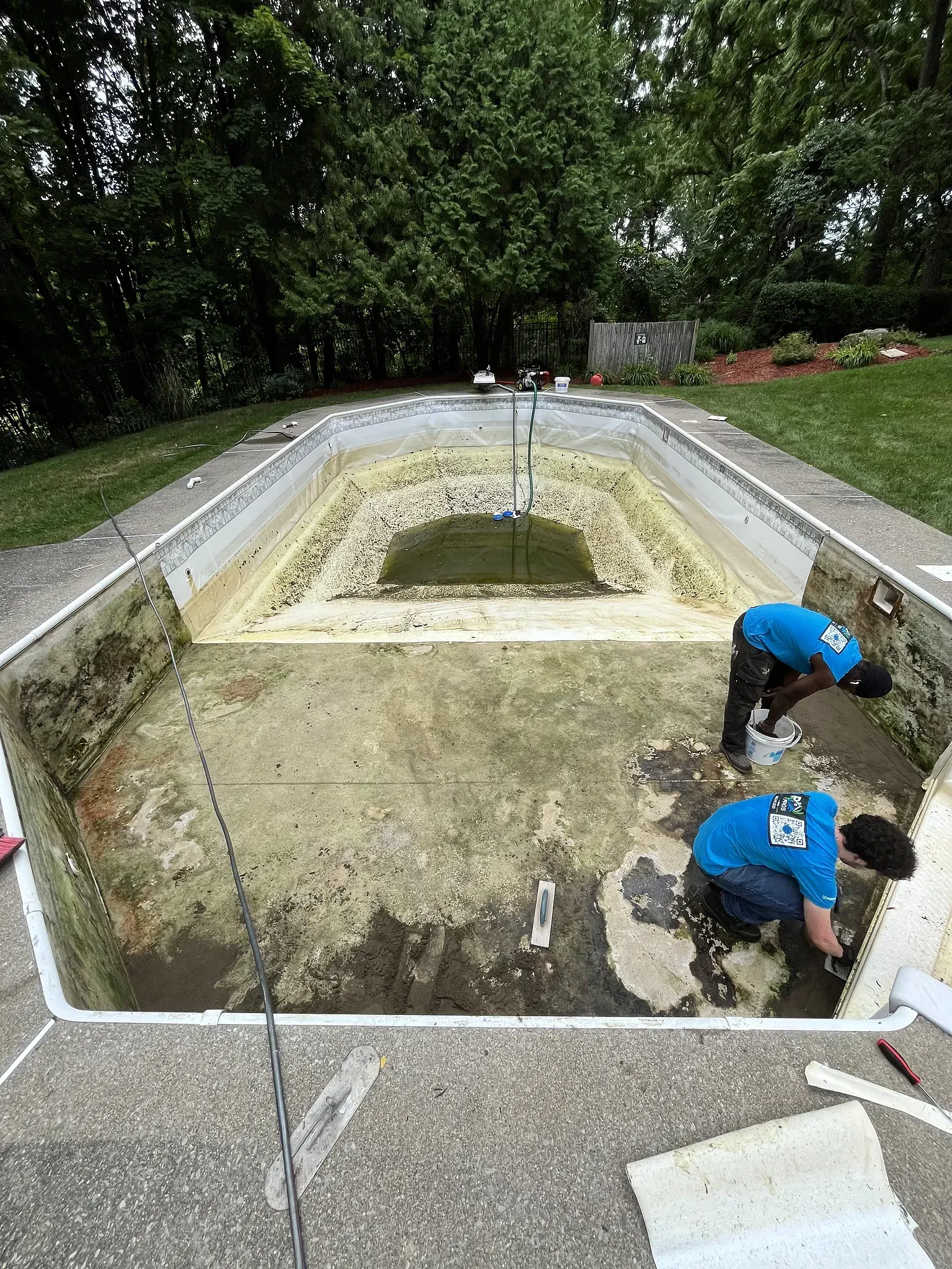 Workers inspect a rectangular stone-lined pond or fountain basin in a park