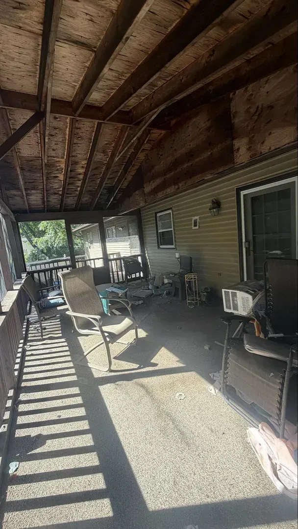 Covered patio with wooden ceiling, chairs, and sunlight casting striped shadows on the floor.