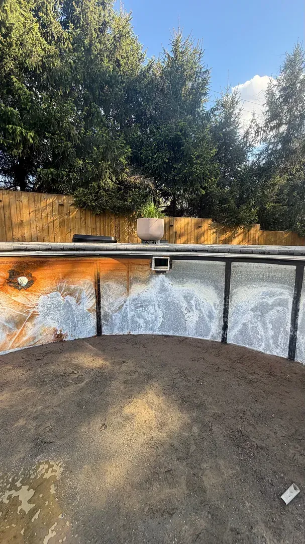 Backyard pool with a weathered wall, surrounded by trees and a blue sky