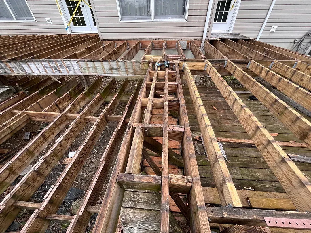 Exposed wooden deck joists and beams during deck demolition beside a house.