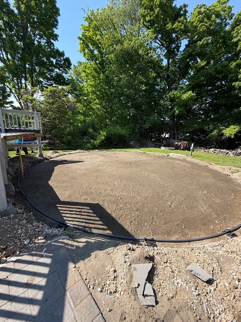 Freshly poured concrete slab in a backyard, bordered by gravel and trees on a sunny day