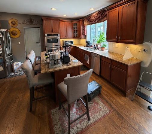 Warm kitchen with wooden cabinets, island seating, granite counters, and sunlight by the window.