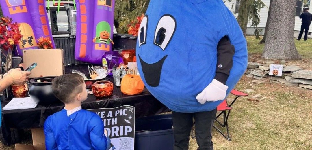 Blue mascot greets a child at a Halloween display with pumpkins and colorful decorations