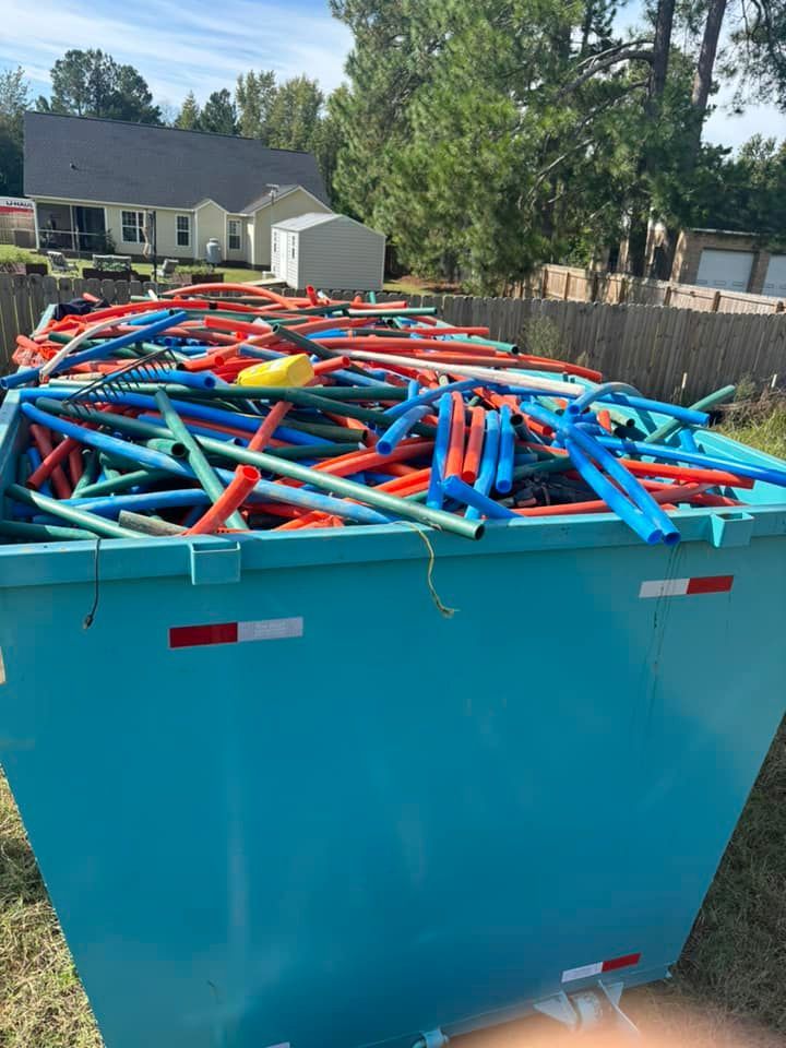 A full, light blue dumpster overflowing with colorful pool noodles in a yard.