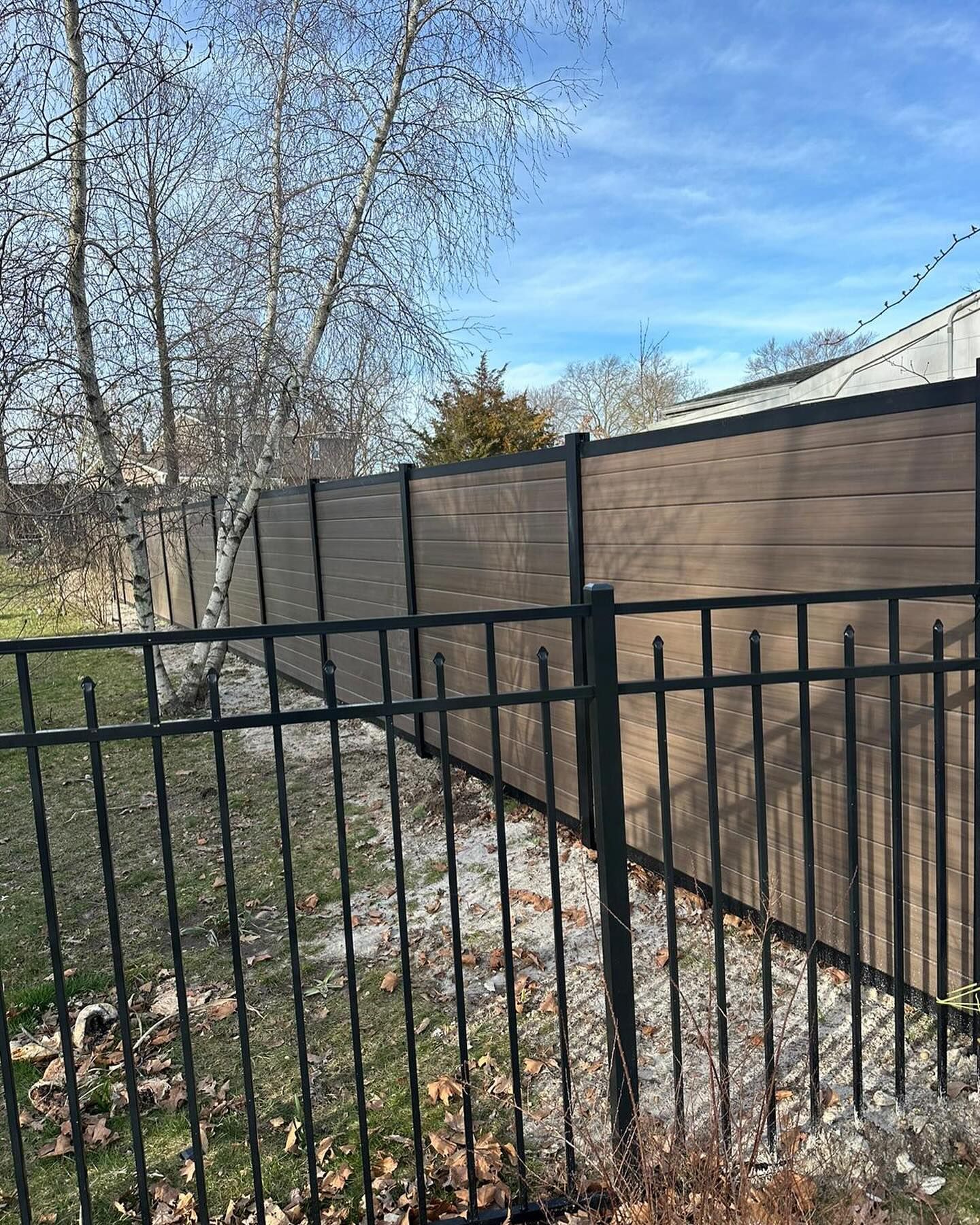 A metal fence with a wooden fence behind it.