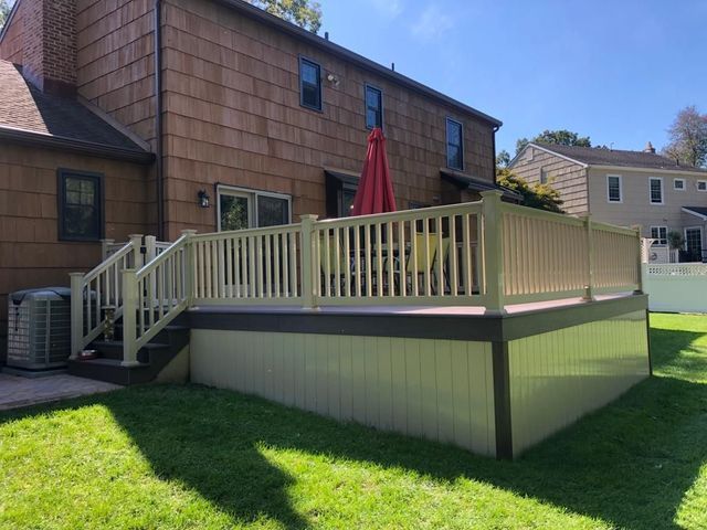 A large deck with stairs and a red umbrella in front of a house.