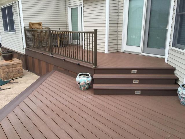 A wooden deck with stairs and a railing on the side of the house .