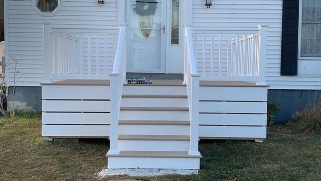 A white house with a porch and stairs in front of it.
