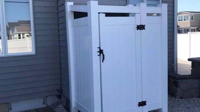 A white shower stall is sitting outside of a house next to a window.