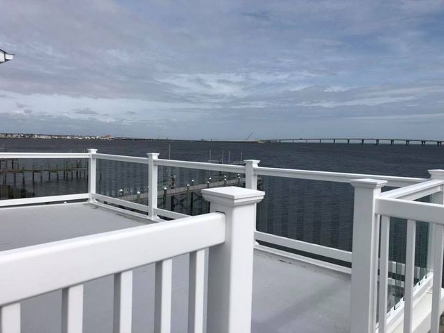 A white railing overlooking a body of water with a bridge in the background.