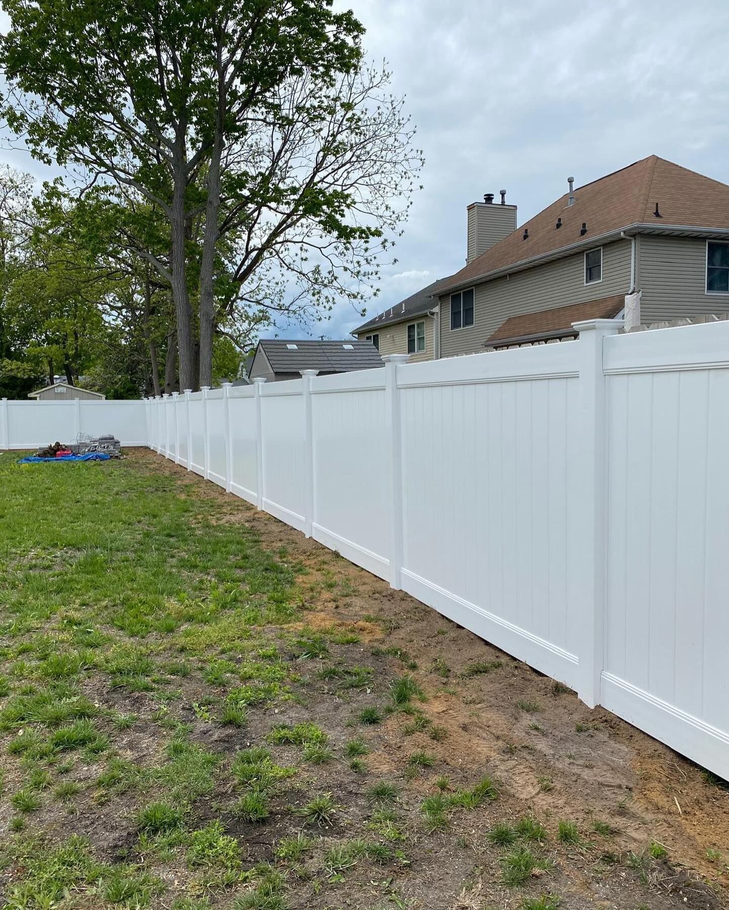 A white fence is surrounding a grassy yard in front of a house.
