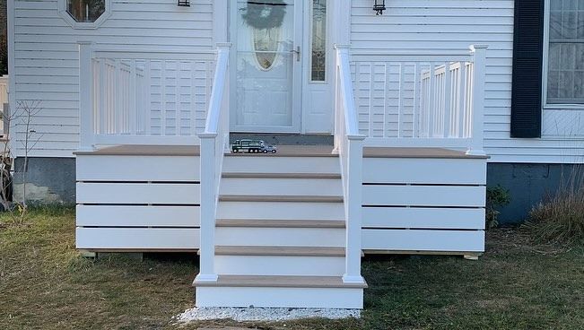 A white house with a porch and stairs in front of it.