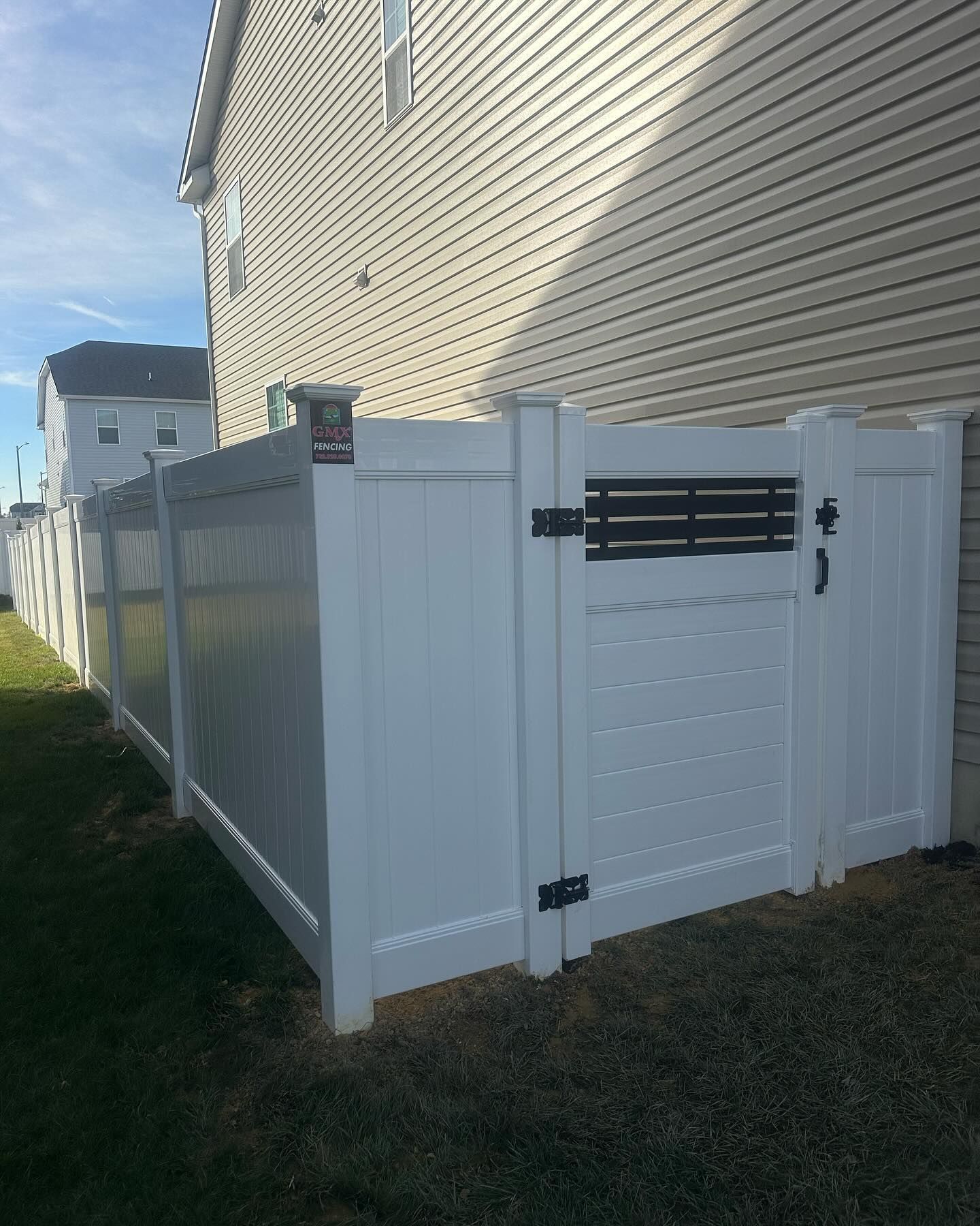 A white vinyl fence with a black accent gate is next to a house.