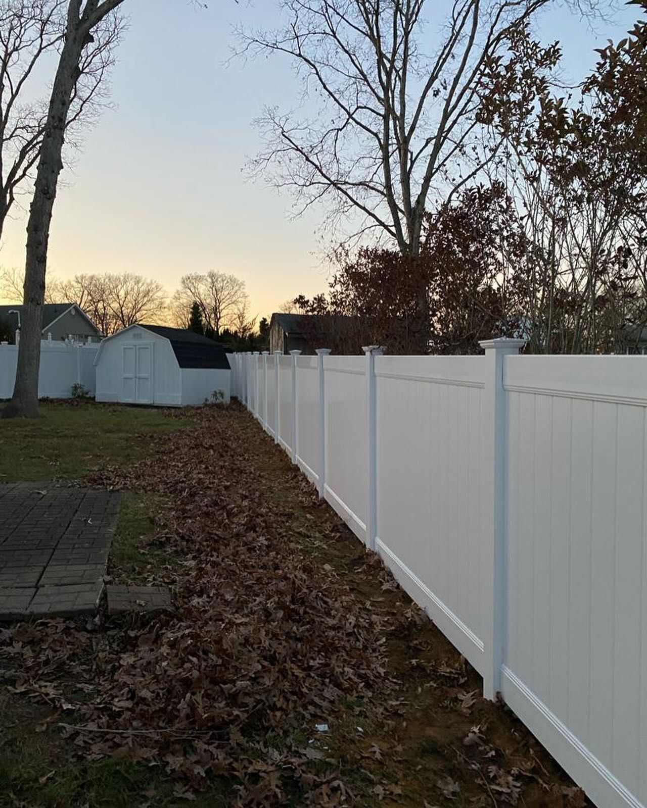 A white fence surrounds a yard with a shed in the background.