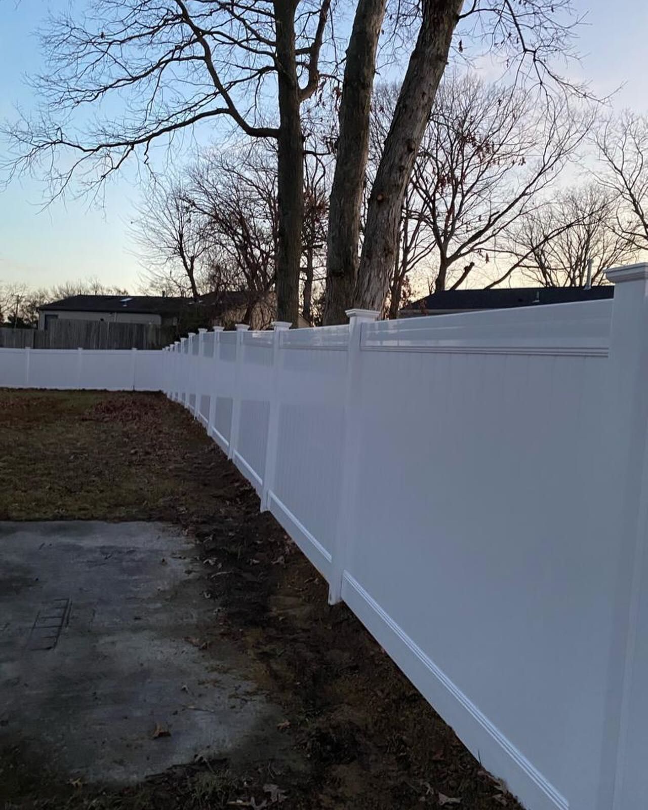 A white fence surrounds a yard with trees in the background.
