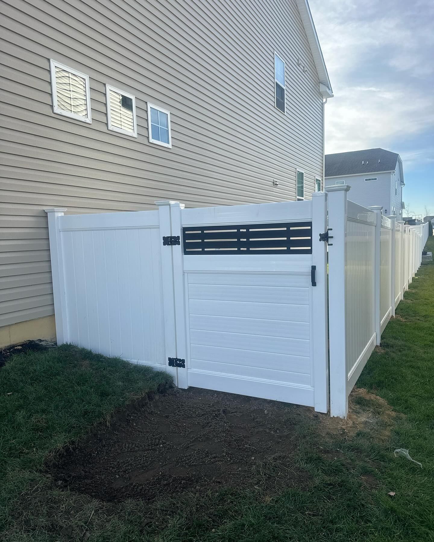 A white fence with a black gate is next to a house.