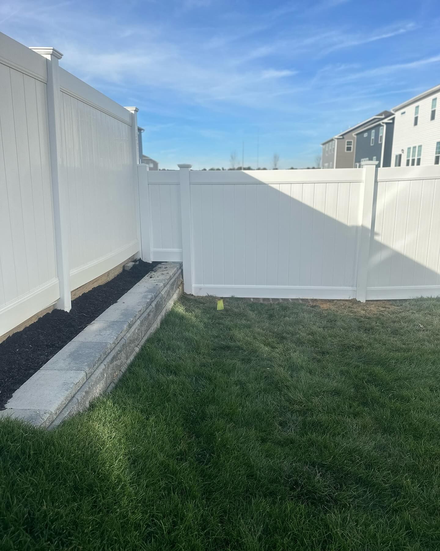 A white fence surrounds a lush green lawn in a backyard.