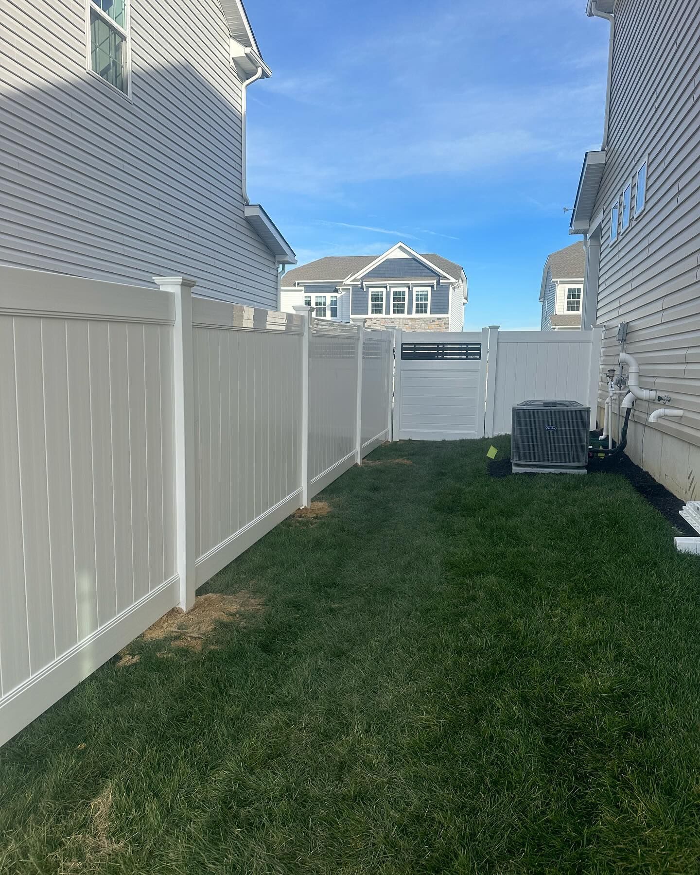 A white fence surrounds a lush green yard between two houses.