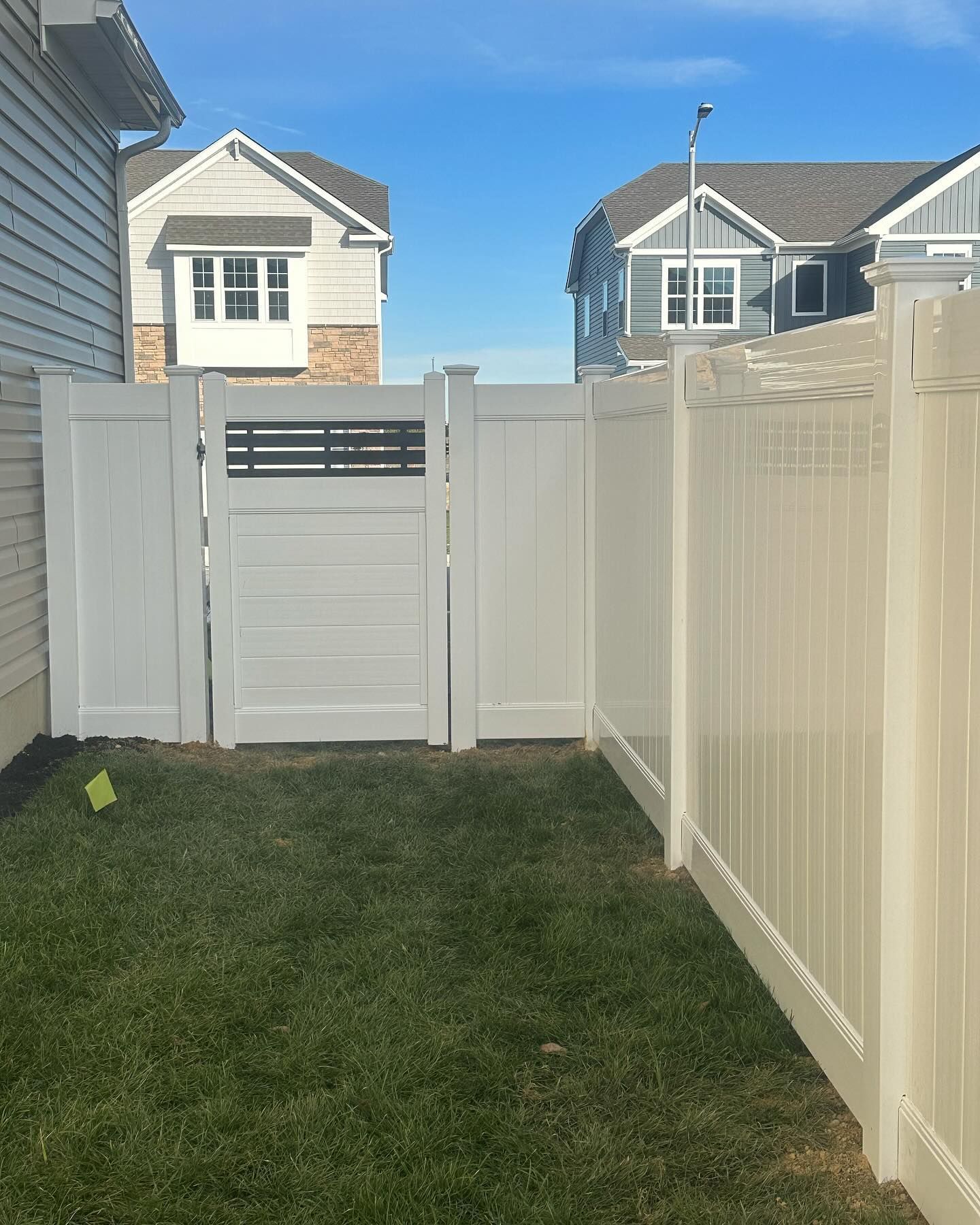 A white fence with a gate in the backyard of a house.
