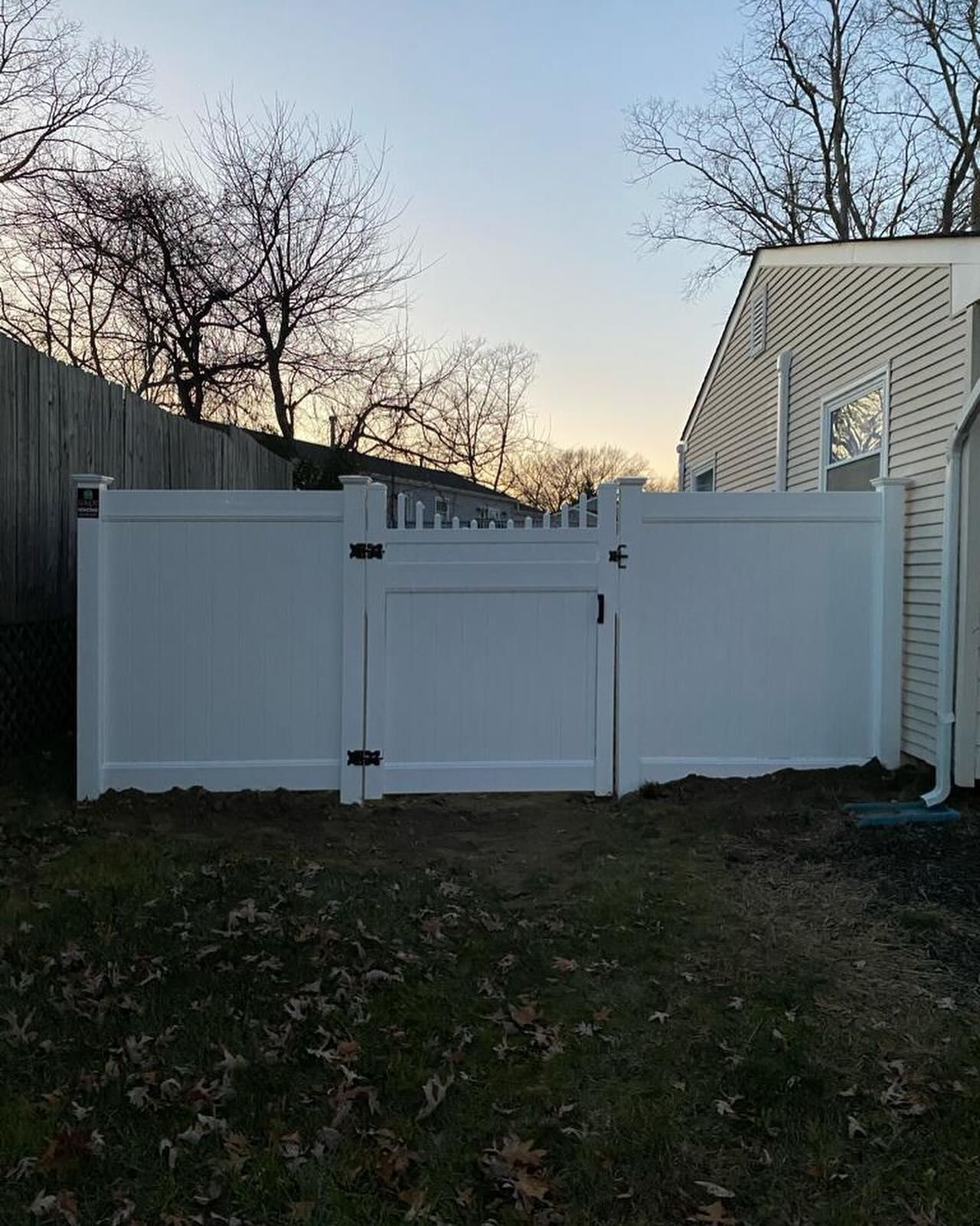 A white fence with a gate in the backyard of a house.