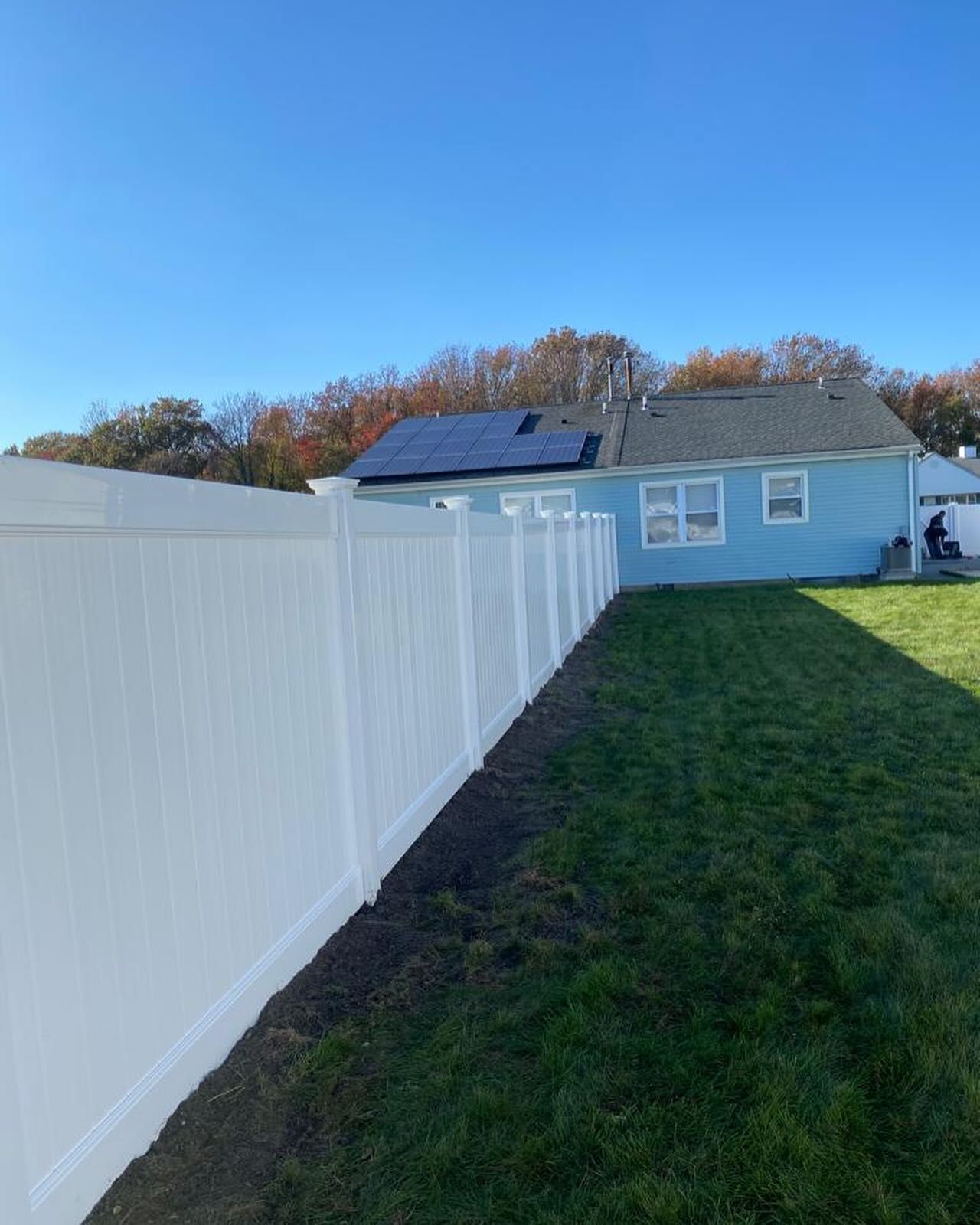 A white fence surrounds a house with solar panels on the roof.