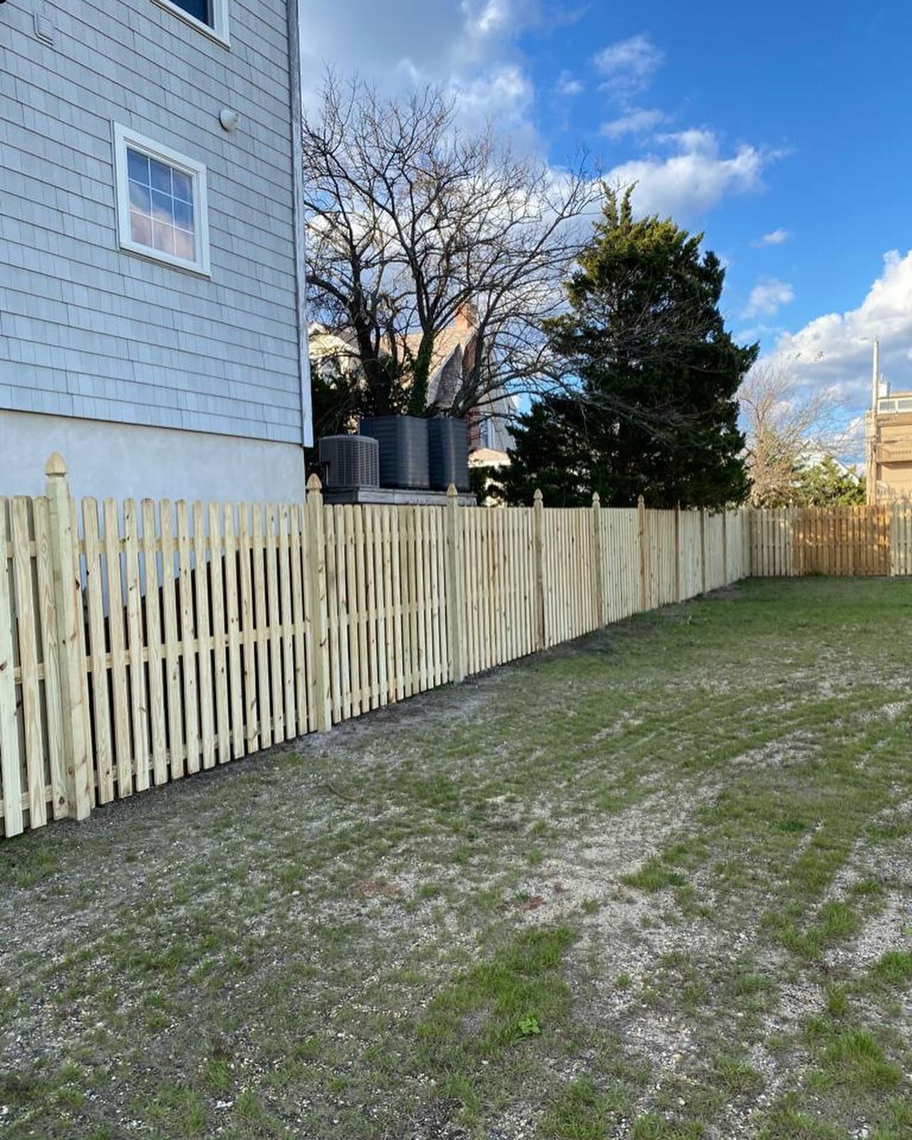 A wooden fence is surrounding a grassy yard in front of a house.