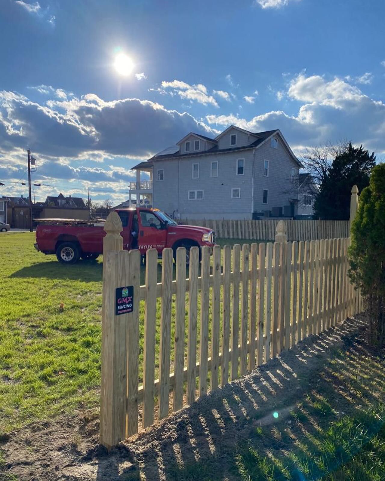 A red truck is parked in front of a wooden picket fence.