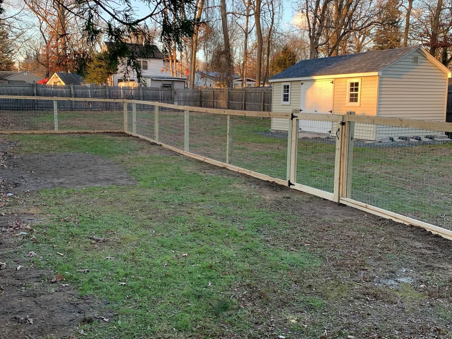 A wooden fence surrounds a lush green yard in front of a house.