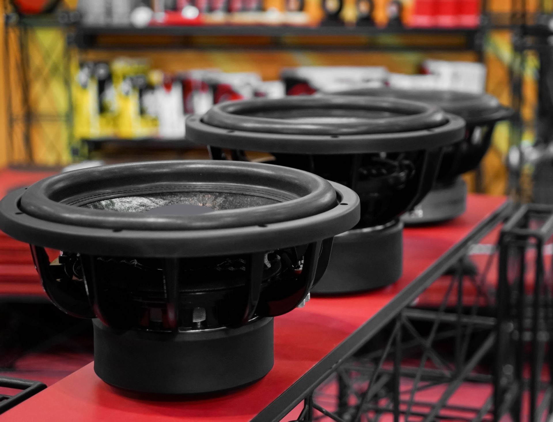 Three black subwoofers lined up on a red surface, blurred store background.