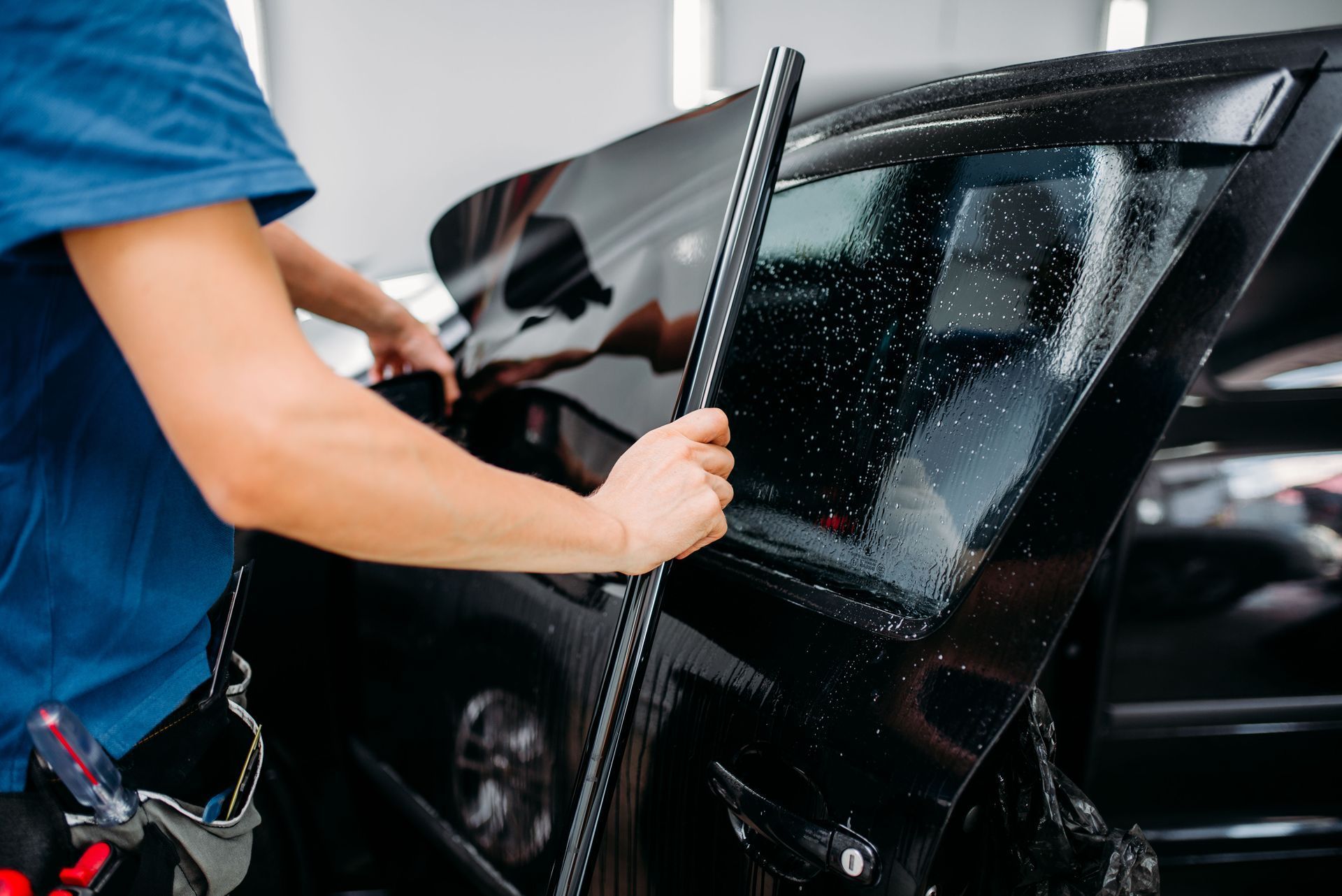 Person installing tinted film on a car window.