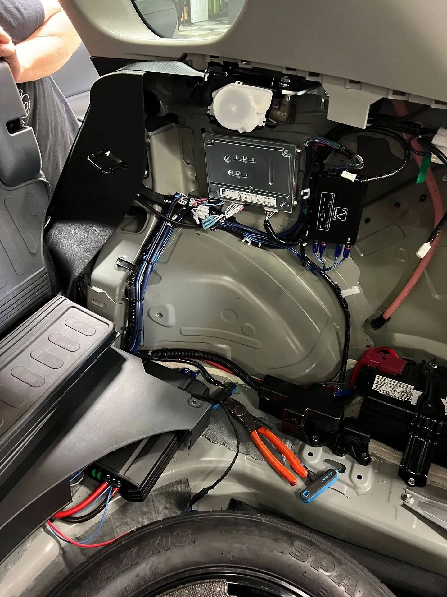 Car trunk interior showing various components, wiring, and tools.