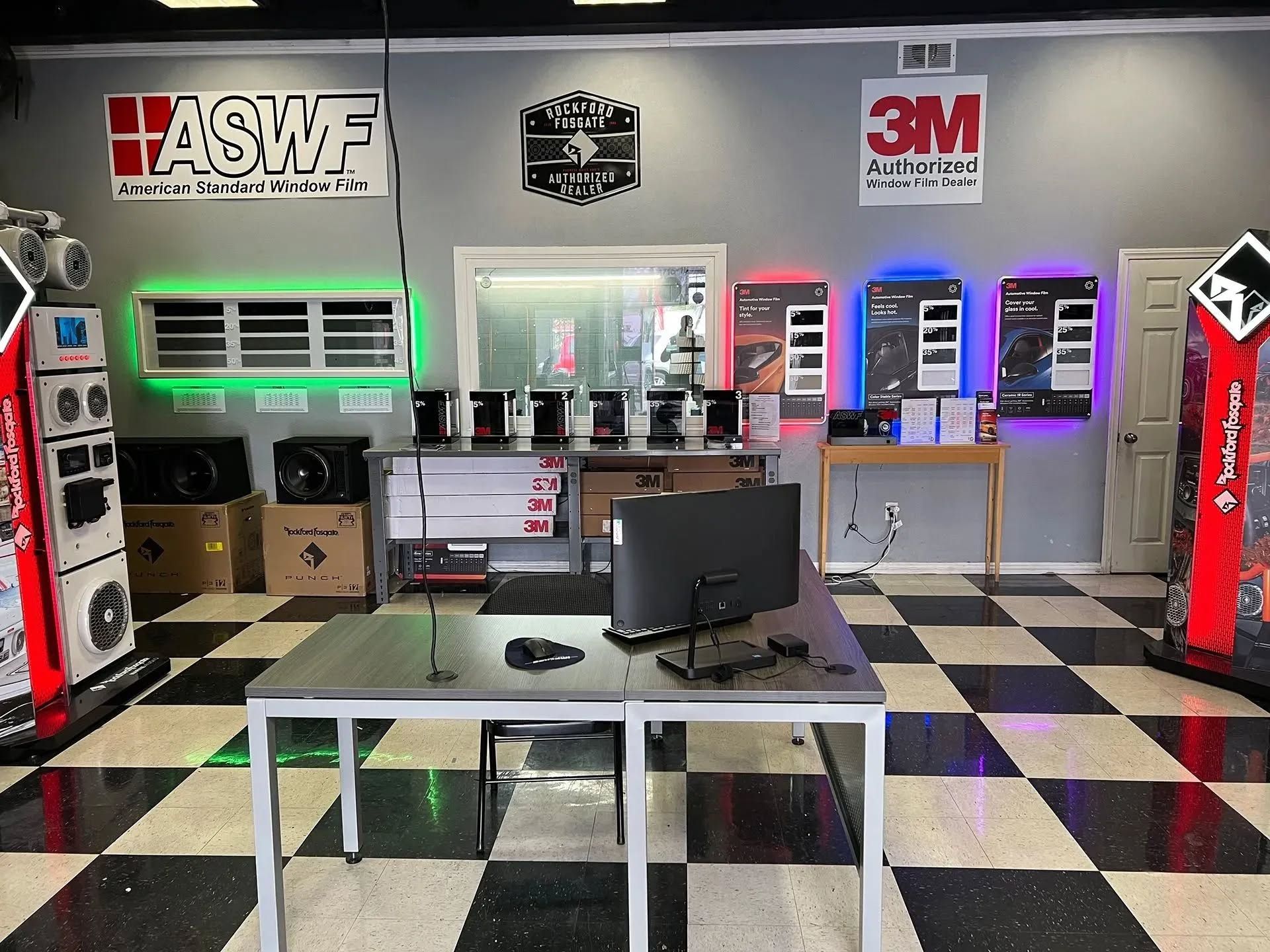 Car audio shop interior with speakers, displays, checkered floor, and computer desk.