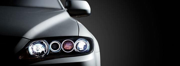 A silver car's headlight assembly with the hood and side mirror visible against a dark gray background.