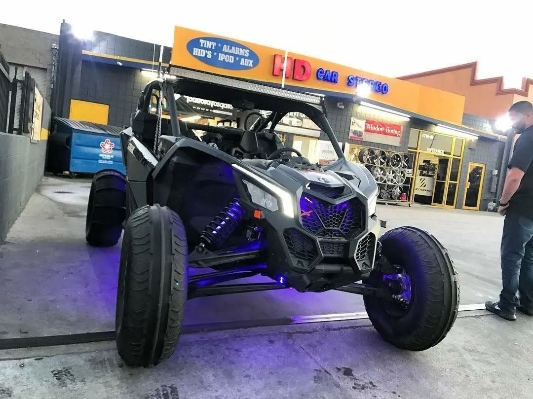 Black and white off-road vehicle with purple underglow parked in front of a store with a blue dumpster.