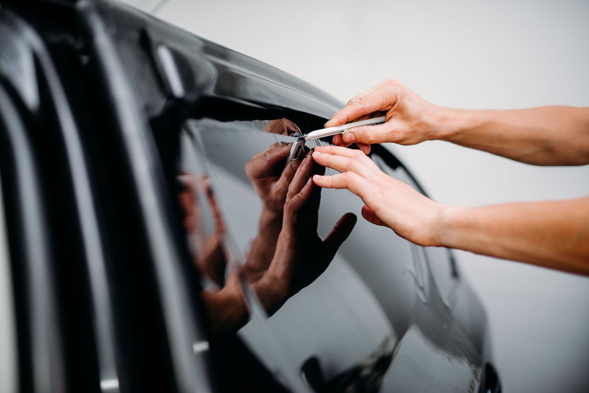 Person using a utility knife to trim window tint on a car window.