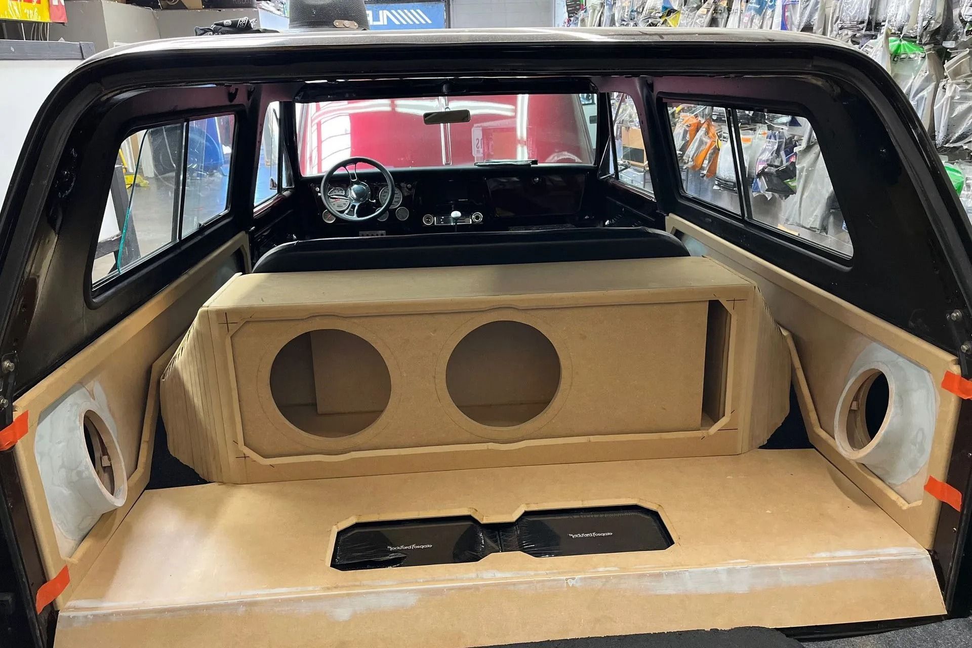 Interior of a truck bed with a custom speaker box and amplifier. Unfinished wood and black interior.