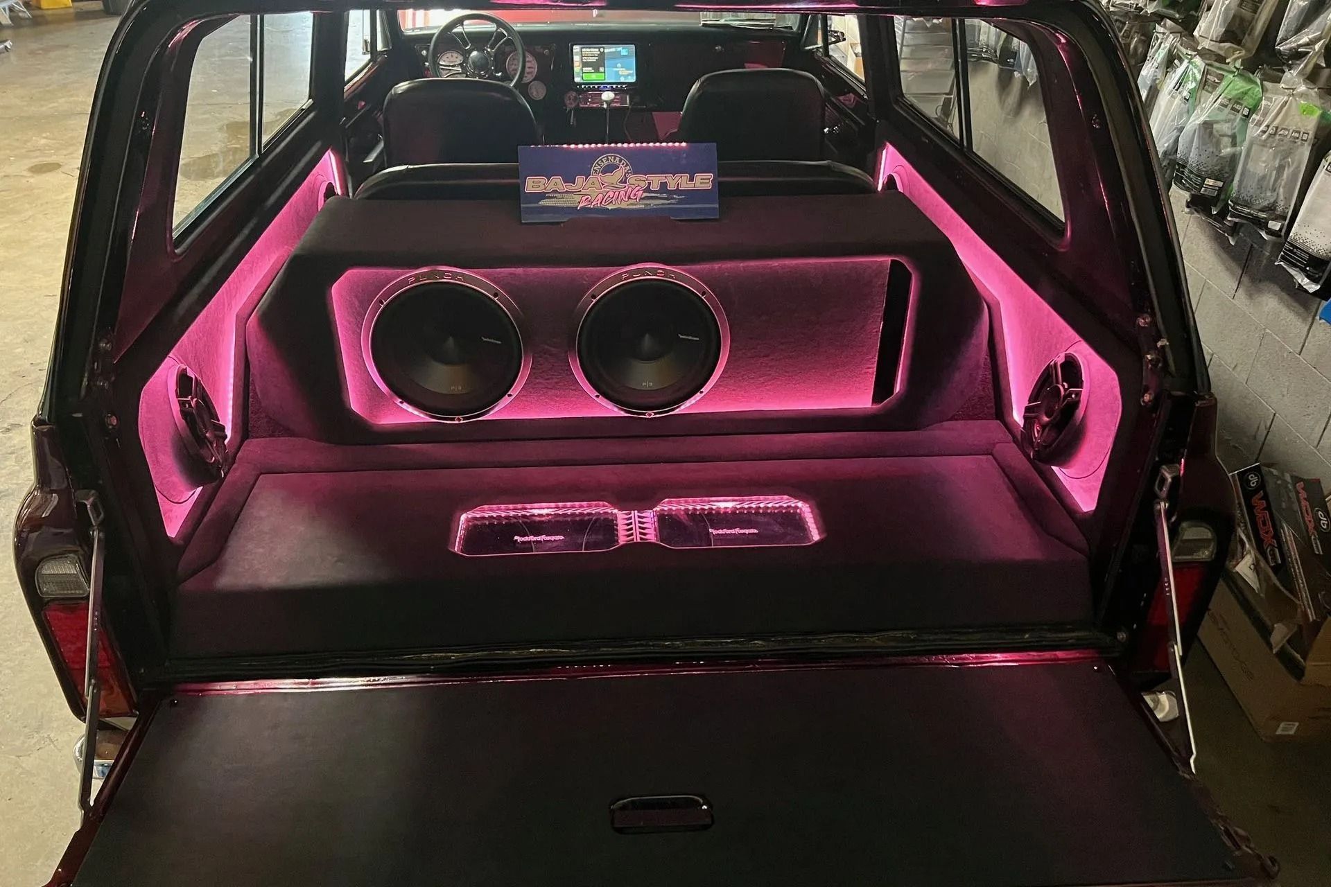 Car trunk interior with custom audio system, lit with pink neon.